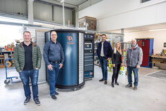 BOOST.Tower Fünf Menschen stehen rund um den BOOST.Tower, ein Beschaffungssystem